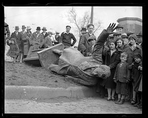 People gathered around a statue on its side