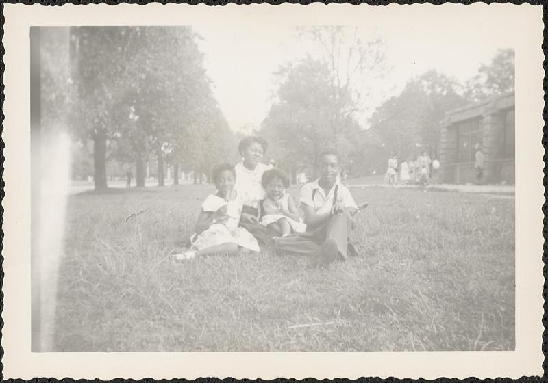 Yvonne sits on grass with two girls and a young man