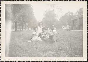 Yvonne sits on grass with two girls and a young man