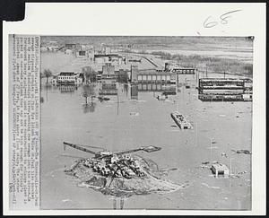 Knocked Out by Flood-The Minneapolis-St. Paul sewage disposal complex on Pigs Eye Island below St. Paul lies knocked out by swollen Mississippi River, sending raw sewage into the stream. In foreground heavy equipment used in new construction to enlarge plant is parked on man-made island that may not be high enough for Friday's predicted crest of 27 feet, 14 feet above flood stage. The stream measured 23.45 feet today.