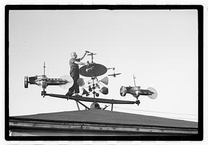 A man adjusting an elaborate device on roof, possibly a weather vane