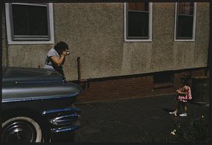 Woman photographing girl in front of a blue car