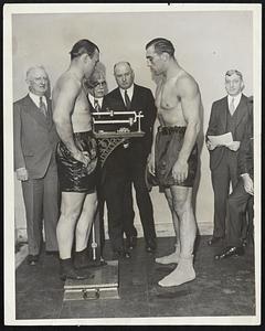 Ready for Clash. Jack Sharkey is shown standing on the sacles in New York Oct. 12 weighing in for his bout with Primo Carnera, Who stands by awaiting his turn to get on the weighing machine. The Boston sailor fought the man-mountain from Italy in Eddets Field, Brooklyn.