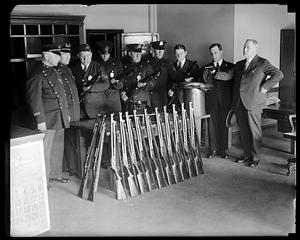 A group of police officers standing behind a row of rifles