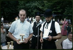 Young man holding a trophy and standing with a bicentennial emcee and another bicentennial attendant