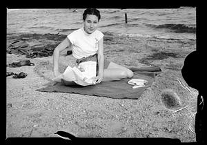 A woman sits on beach with a newspaper