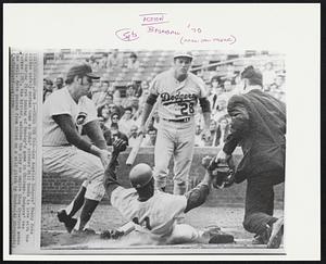Under the Tag -- Los Angeles Dodgers' Manny Mota slides safely across home as Cubs' pitcher Bill Hands is late with the tag during first inning of Monday's game in Chicago. Dodgers' Wes Parker (28), the hitter, watches the play as umpire Shag Crawford makes the call. Mota scored from third on a wild pitch by Hands.