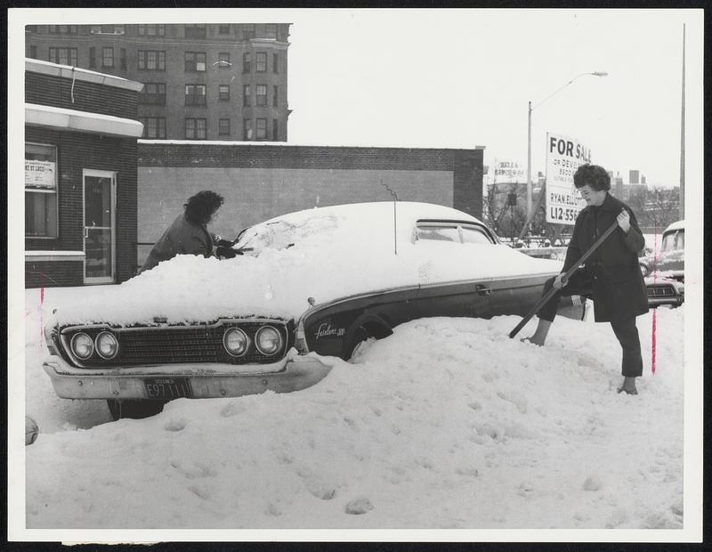 Clearing white Christmas off their cars are Marry Merril, of Back Bay (left) and Mary Cellucci, of Newton, who seem to be saying “Who Needs it?”.