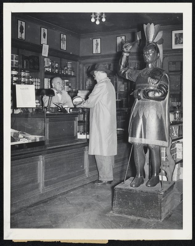 Wooden Indians Near End of Trail. Oblivious to the wooden Indian whose tomahawk menaces from behind, a customer orders tobacco from James B. Russell, New York City retailer. Mr. Russell, who got the Indian 16 years ago, bought it from a man in Monticello, N.Y., who had it for 10 years before the present owner acquired it.