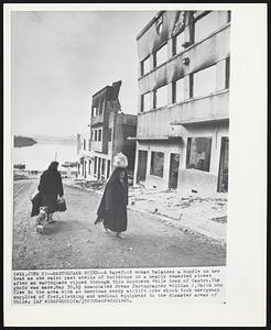 Earthquake Ruins -- A barefoot woman balances a bundle on her head as she walks past shells of buildings in a nearly deserted street after an earthquake ripped through this southern Chile town of Castro. The photo was made, May 30, by Associated Press Photographer William J. Smith who flew to the area with an American mercy airlift crew which took emergency supplies of food, clothing and medical equipment to the disaster areas of Chile.