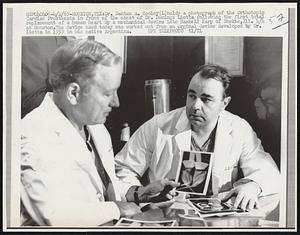 Dr. Denton A. Cooley (L) holds a photograph of the Orthotopic Cardiac Prosthesis in front of the chest of Dr. Domingo Liotta following the first total replacement of a human heart by a mechanical device into Haskell Karp of Skokie, Ill. 4/4 at Houston. The device used today was worked out from an original device developed by Dr. Liotta in 1959 in his native Argentina.