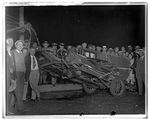 People stand by a wrecked car about to be towed away
