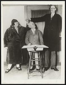 Signing Them Up For Life. “Cupid” Grant Munson, marriage license clerk of San Francisco, Calif., who stands but 5-foot 3-inches high, felt himself in strange company when John Greech, 46-year-old Oklahoma giant, standing 8-foot 6-inches tall, applied for a license to marry Miss Grace Carlisle, 18, 5-foot 6-inches and weighing 600 pounds. They will be married by superior judge Louis H. Ward, 5-foot 6-inches, the smallest superior judge in the state.