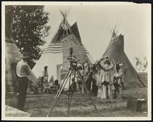 The motion picture camera is here shown as it stood ready to undertake on of the strangest jobs ever assigned to it--the photographing of a language. In front of the camera area seen some of the Indian chiefs who met in a special council at Browning, Montana, to provide a permanent photographic record of their significant hand-wavings.