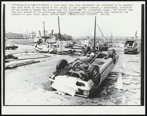 Cincinnati: A late model cars lies overturned and abandoned on an expressway exit where it was hurled at the height of last night’s tornado. A restaurant, destroyed by the storm is beyond the downed sign and Interstate 75, background right. The entire area has been sealed off by police and National Guardsmen who are allowing only residents and workers to pass their lines.