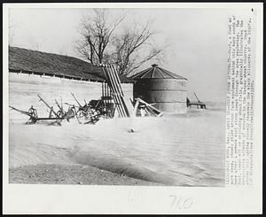 Dust Storm Aftermath--Dust, a foot or more deep, stands piled around farm equipment behind this barn south of here after a severe dust storm swept through the area yesterday. The dust, swept off an adjoining wheat field, graphically illustrates the devastating effects of erosion in the Kansas wheat country. Dust storms this spring closely resemble the black blizzards of the 1930's.