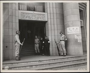 Both GI and Japanese police stand guard at the entrance to the Tokyo Police Hqrs., which also serves as the hqrs. for the 1st Cav. Div. M.P. Platoon