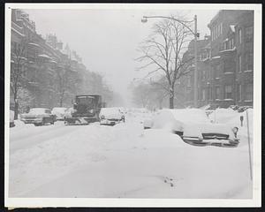 It Looks Like A Parking Lot, but this really is heavily-traveled Beacon-street in the Back Bay. But traffic is reduced to a crawl and a big snow plow can barely clear one lane as motorists abandoned cars in the middle of the street. Car in foreground has been snowed in since first storm a week ago.