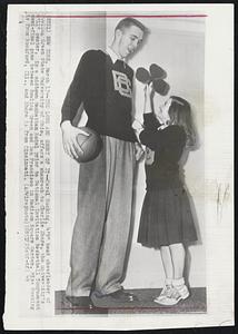 The Long and Short of It-- Carol Hocking, 4'9" head cheerleader of Bowling Green State University of Ohio, offers a shamrock to Charlie Share, the university's 6'11" center, in a midtown Manhattan hotel prior to National Invitation Basketball Tournament semi-final game between Bowling Green and San Francisco in Madison Square Garden. Miss Hocking is from Rockford, Ill., and Share is from Cincinnati.