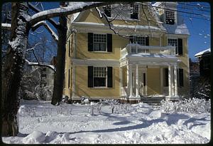 Snow in front of yellow house with dark shutters