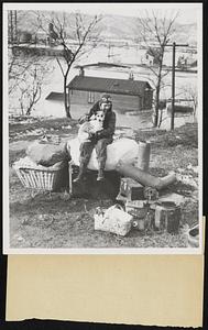 Holding his dog in his lap, this 15-year-old lad surveys his possession saved from the house shown partly submerged in the background as he calmly awaits a rescue boat