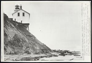 Sea Dooms Lighthouse-This 80-year-old North Cove lighthouse, its south wall cut away by sea, stood precariously on cliff today as sightseers waited for waves to undermine remaining foundation.