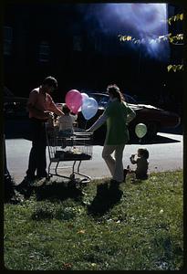Two children with balloons, one sitting in a shopping cart, Boston Columbus Day Parade 1973