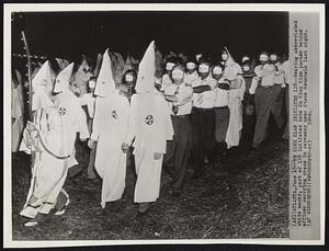 Ku Klux Klan Initiates 128--Wearing abbreviated white masks, part of 128 initiates into Ku Klux Klan parade behind officer carrying cross in ceremony near Stone Mountain last night.