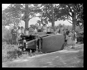People standing by an overturned car on its side