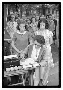 Two young women looking down at a woman signing a piece of paper