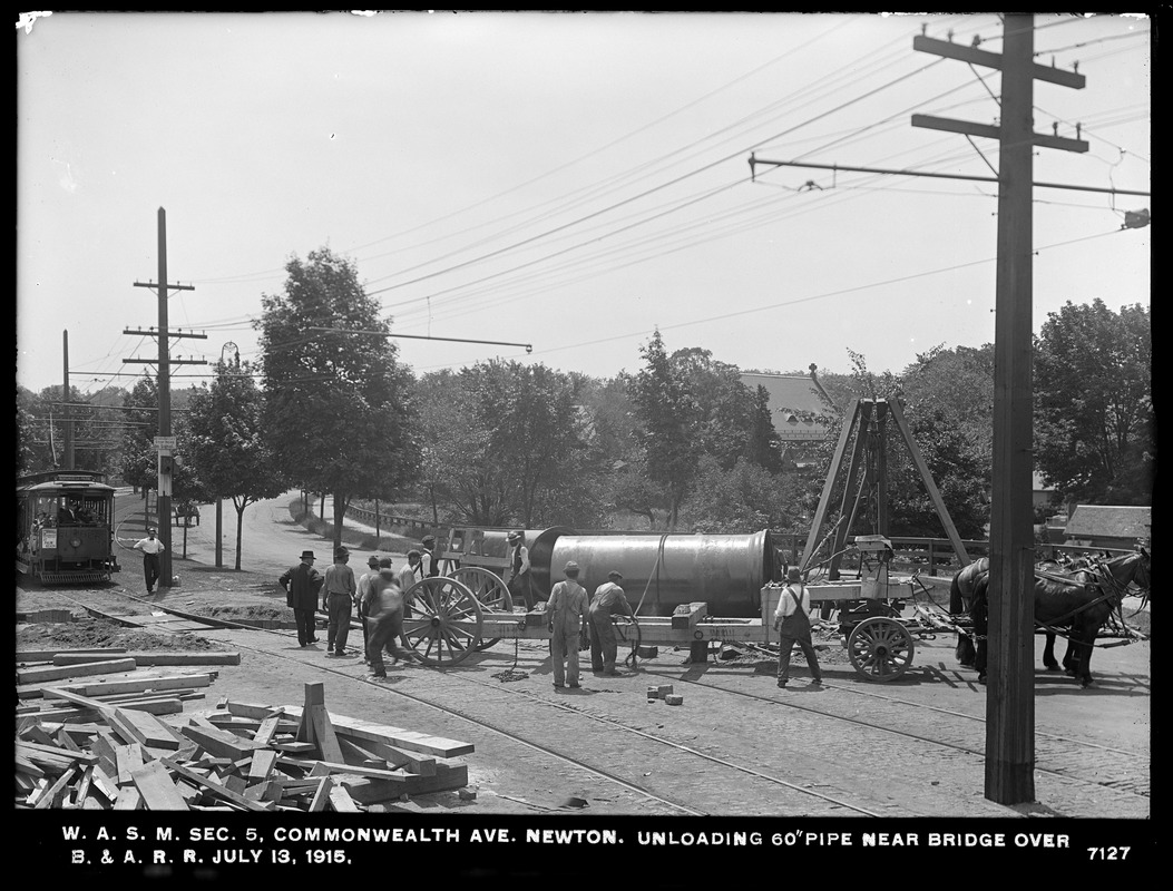 Distribution Department, Weston Aqueduct Supply Mains, Section 5, unloading 60-inch pipe near bridge in Commonwealth Avenue over the Boston & Albany Railroad, Newton, Mass., Jul. 13, 1915