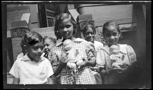 A group of children, two girls in front holding dolls