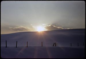 Sun rising or setting over snow-covered hill