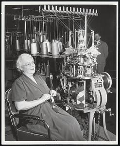 Grandma and the Machine Age Grandma (Mrs. E. Lightfoot, 103 South Elberon, Atlantic City) "sticks to her knitting" beside an intricate new hosiery machine exhibited by Scott and Williams, Inc., Laconia, N.H., at the Knitting Arts Exhibition in Atlantic City, April 30 to May 4. The machine almost precisely copies the movements of grandma's nimble fingers in knitting a sock. In the time that her fingers take to go once around the stockings, the machine has knitted a whole sock and is ready for another despite the fact that many colored yarns are used and the pattern is complicated.