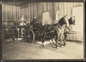 Henry Lakin at reins of steam pumper fire engine, drawn by a pair of horses