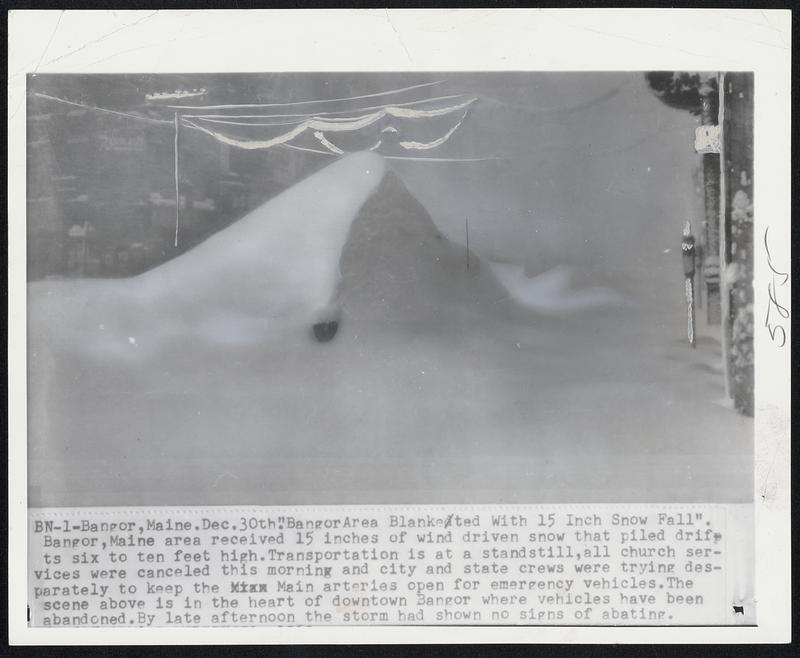 Bangor, Maine. "Bangor Area Blanketed With 15 Inch Snow Fall". Bangor, Maine area received 15 inches of wind driven snow that piled drifts six to ten feet high. Transportation is at a standstill, all church services were cancelled this morning and city and state crews were trying desperately to keep the Main arteries open for emergency vehicles. The scene above is in the heart of downtown Bangor where vehicles have been abandoned. By late afternoon the storm had shown no signs of abating.