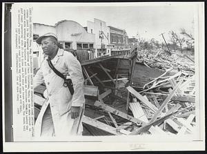 Business Section in Shambles--A local police official stands guard in the downtown section of Pass Christian, Miss. as the main street is covered with wreckage from business and beach homes as hurricane Camille lashed the gulf coast yesterday with 20 foot tides and 180 mile per hours winds. The death toll in Camille's wake stands at over 100 and may reach as high as 200 dead.