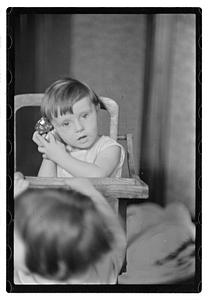 A toddler in a high chair holding an alarm clock