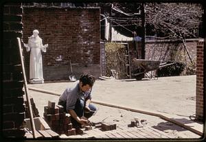 A man laying brick in the courtyard of the Old North Church, statue of St. Francis of Assisi in the background