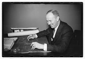 A man seated at a desk, blueprints in front of him