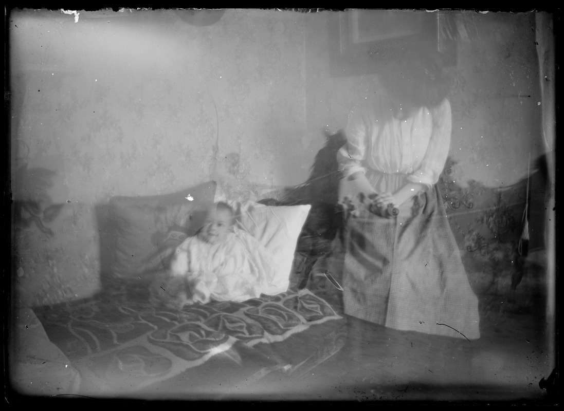 Interior. Woman standing, baby on bed - quilt?