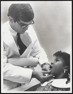 Examining Patient who took part in Tufts-Columbia Point Health Center pilot dental project is Dr. Richard H. Ferraro, director of a planned dental health facility. Opening wide is a 7-year-old patient, Ava Hurd.