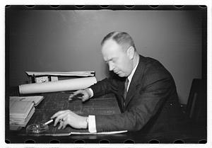 A man seated at a desk, blueprints in front of him