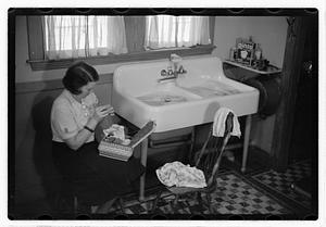 A woman sewing next to a sink full of laundry