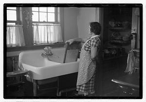 A woman standing by a sink holding a washboard