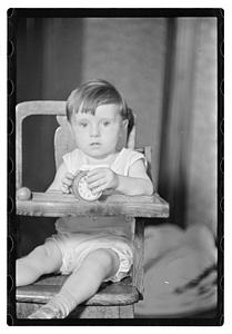 A toddler in a high chair holding an alarm clock