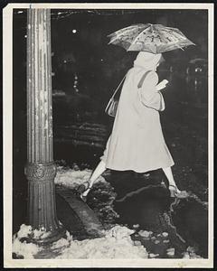 A woman steps across puddle holding an umbrella