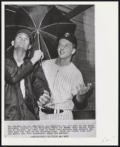 Umbrellas and raincoats are not part of the usual equipment issued to the Minnesota Twins for their Spring training in Orlando, but they came in handy this morning when squally weather kept the team in the dressing room. From the locker room door Joe Kaiser and Fred Bruckbauer check the weather.