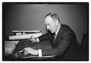 A man seated at a desk, blueprints in front of him