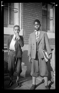 Two boys stand posing, one holding books